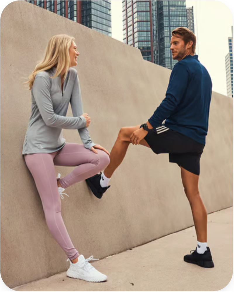 Two people in athletic wear stretching outdoors with a cityscape background