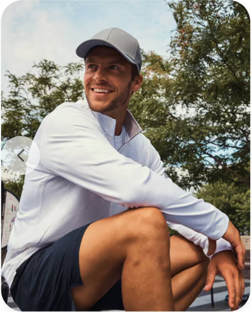 Man in white shirt and cap sitting outdoors with trees in the background