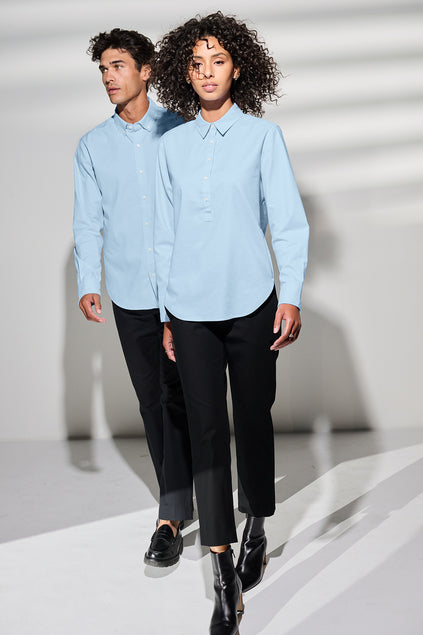 Two people wearing light blue shirts and black pants on a white background