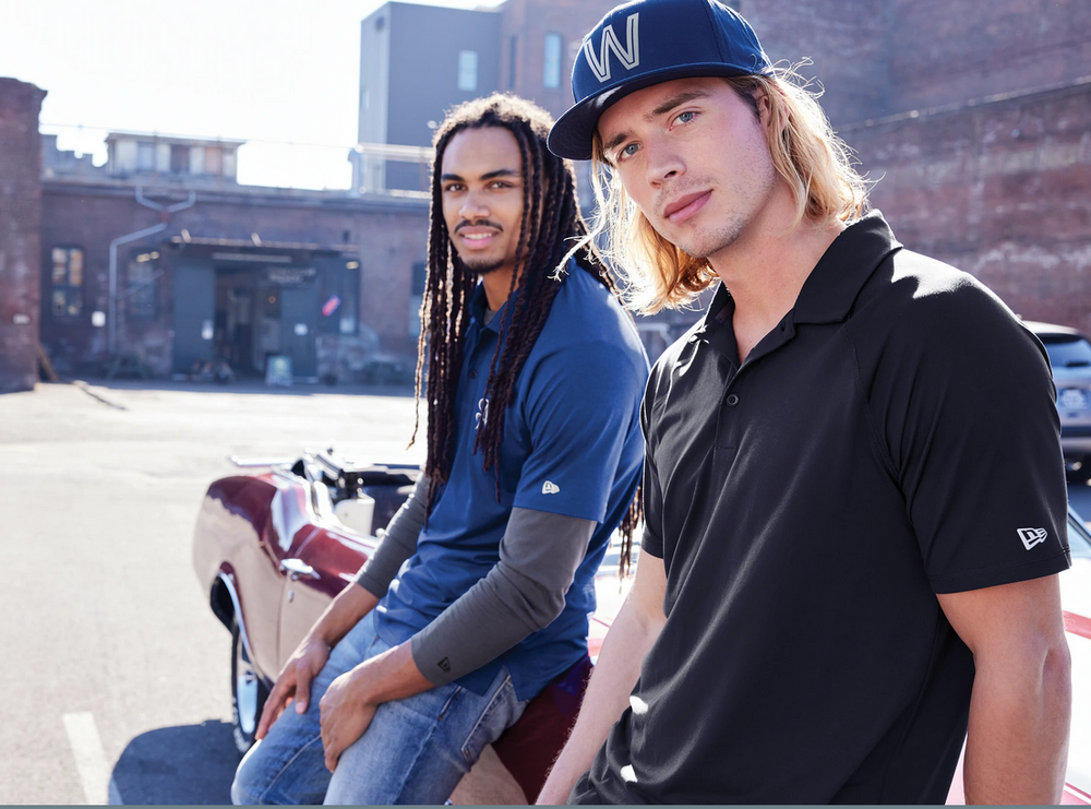 Two men sitting outdoors with a motorcycle, wearing branded clothing and hats.